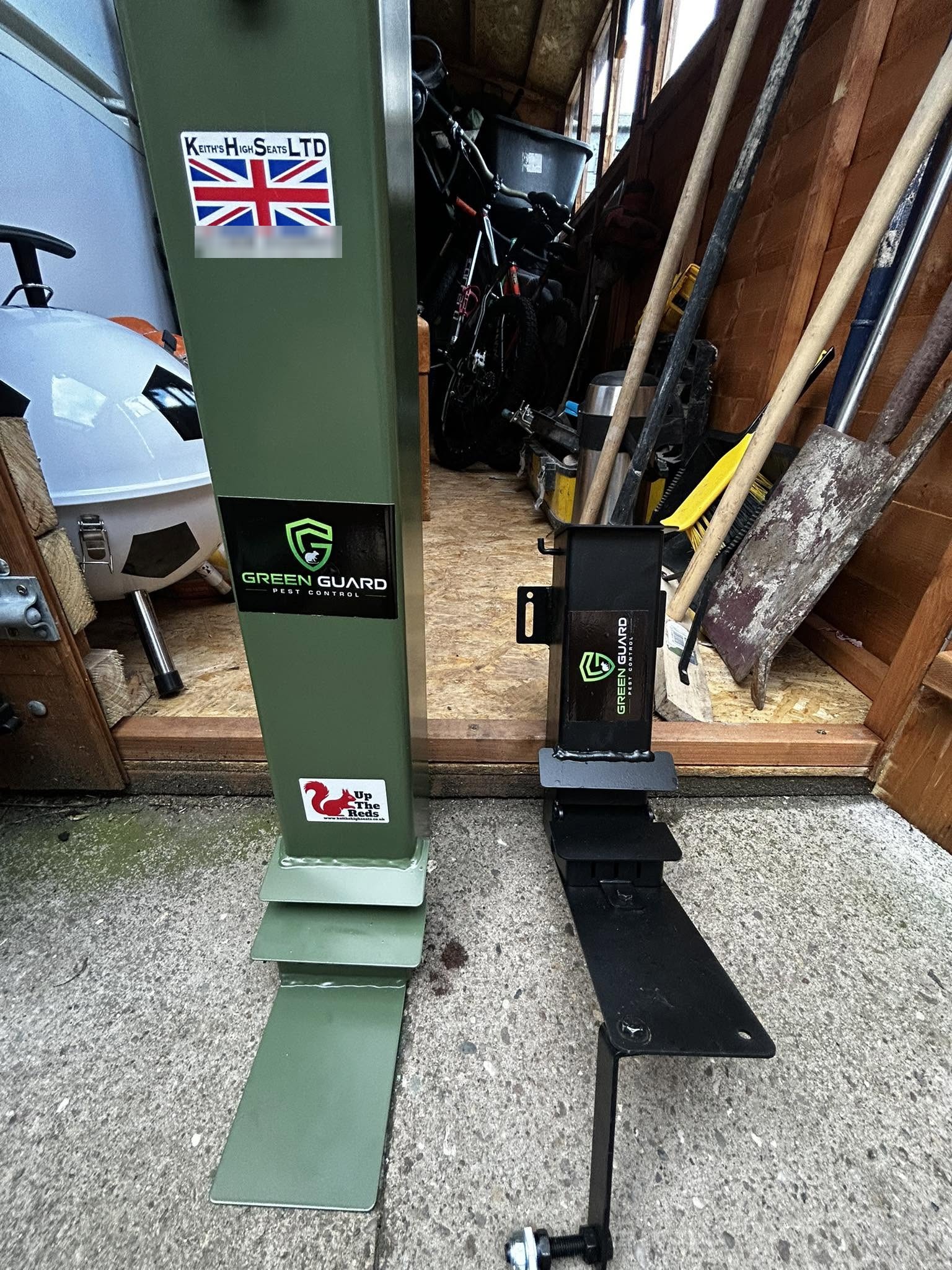 A green squirrel feeder post with a Green Guard Pest Control sticker, standing in a shed