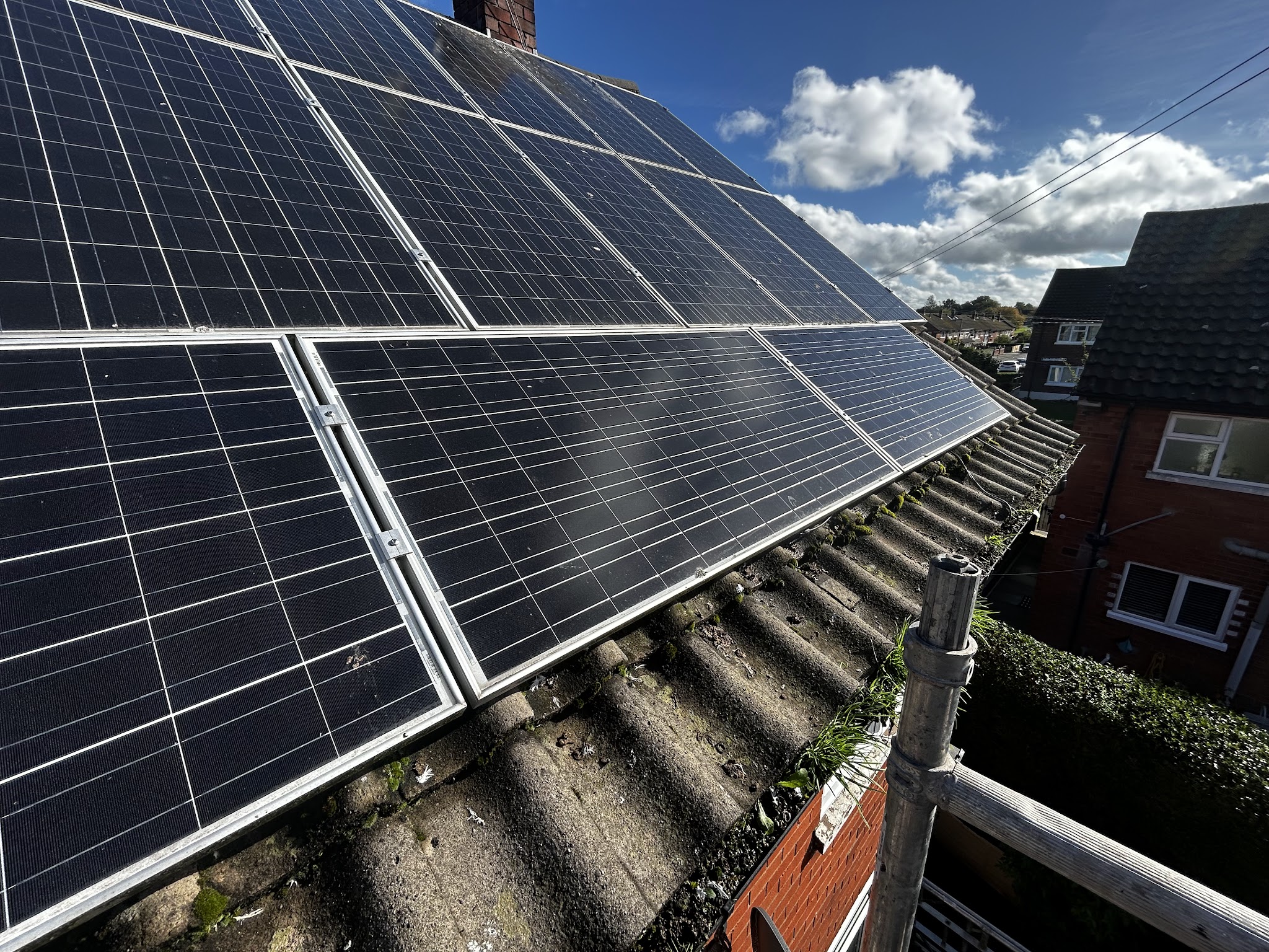 Solar panels on a house roof, seen from scaffolding, with blue sky behind