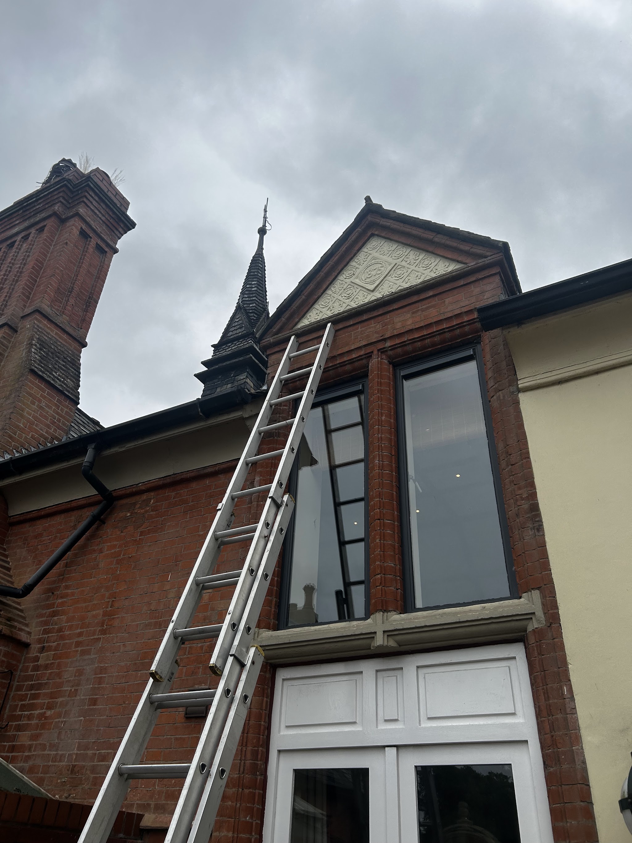 A ladder against the brick front of a Victorian building with a spire behind it