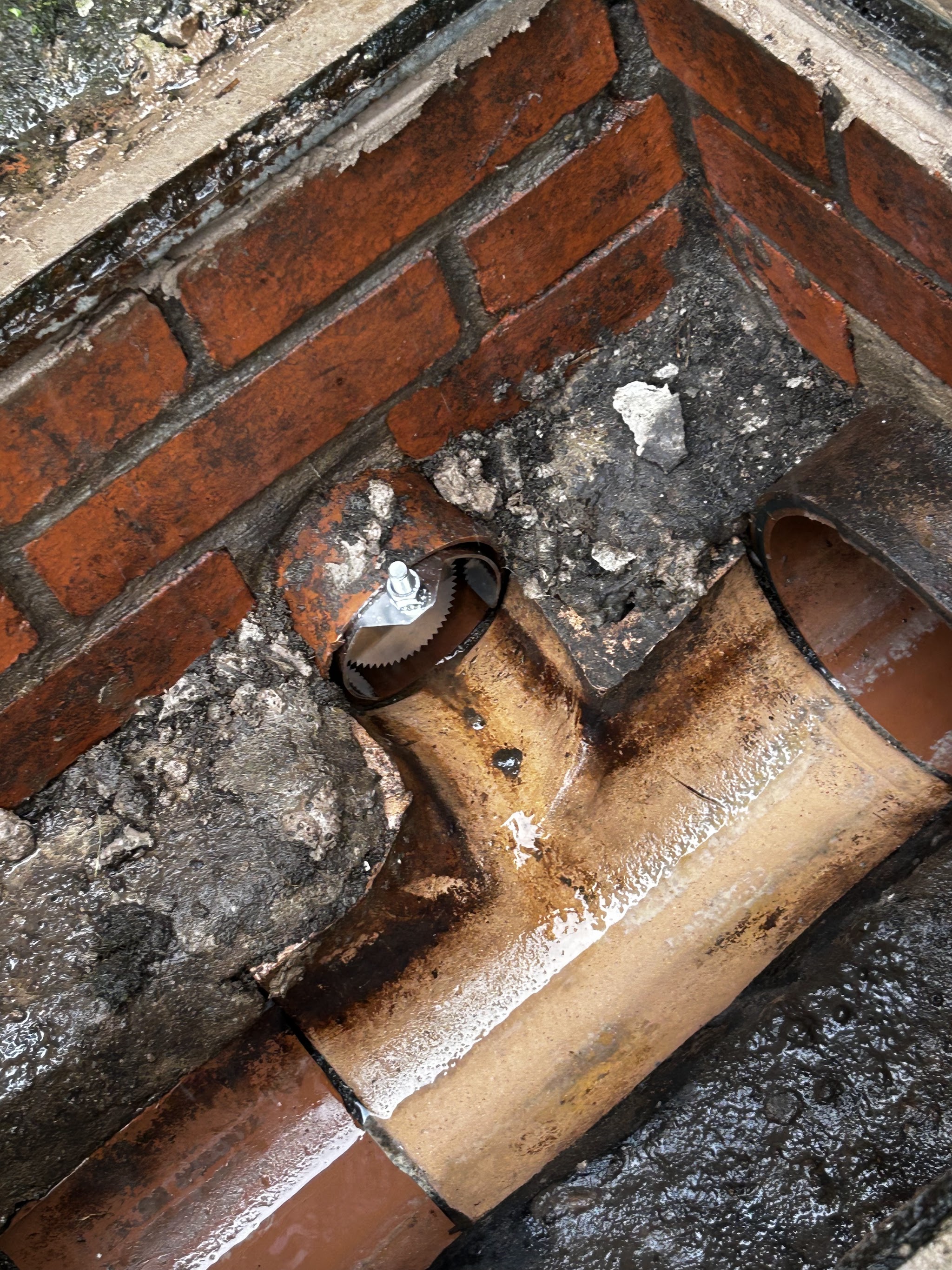 A broken clay drain junction against a brick wall, with an open pipe end